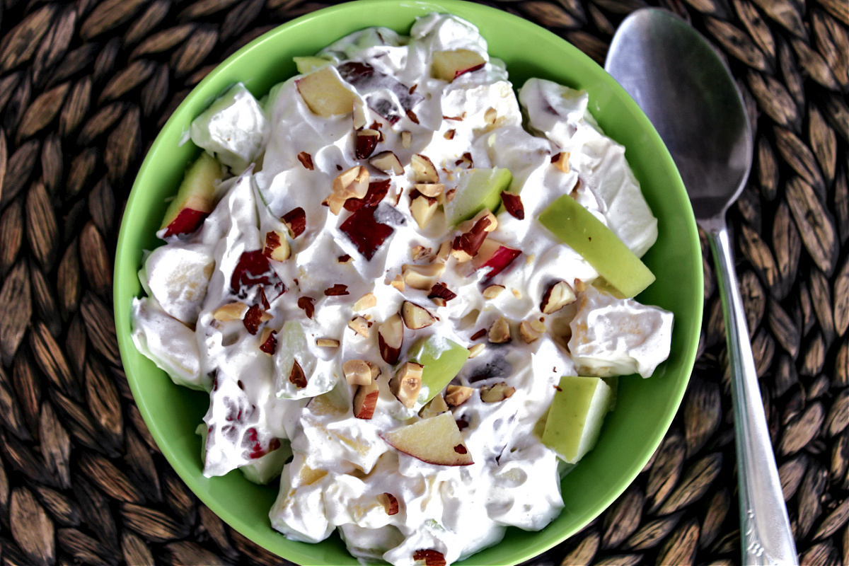 creamy apple salad in a green bowl with a spoon besides. 
