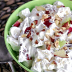 creamy apple salad in a green bowl with nuts on top.