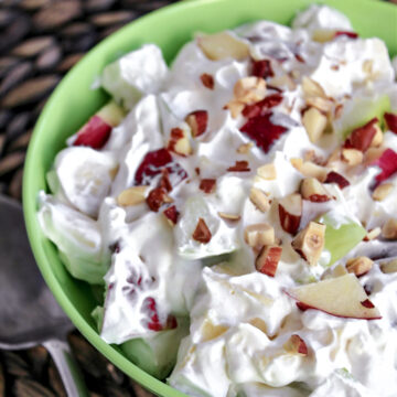 creamy apple salad in a green bowl with nuts on top.