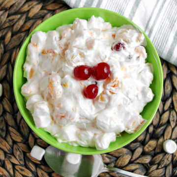 easy ambrosia salad in a green bowl with cherries on top.