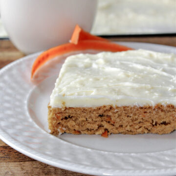 carrot cake on a white plate with carrots behind.