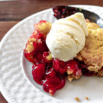 cherry dump cake on a white plate with a spoon behind.