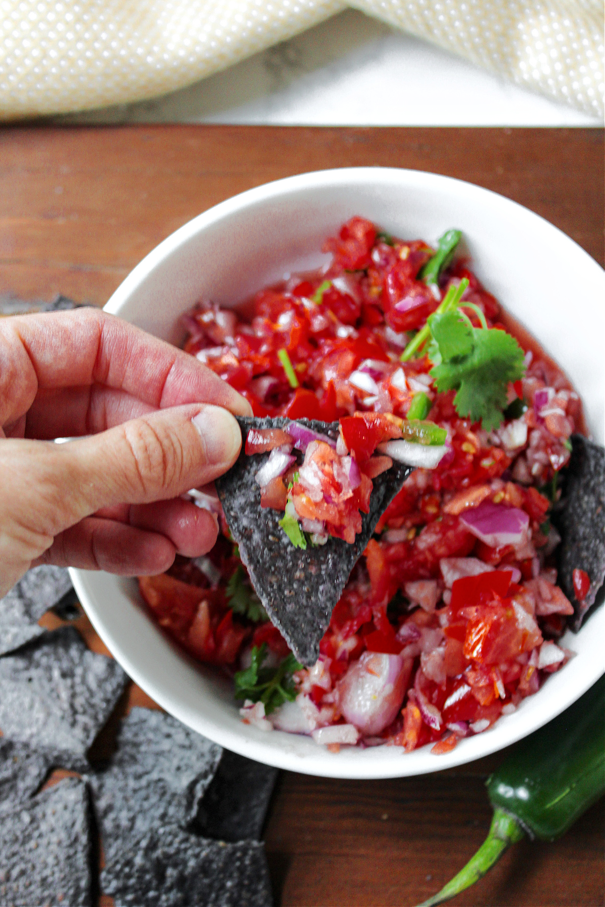 a hand holding a chip with Pico de Gallo on it. 