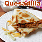 BBQ Chicken Quesadilla on a white plate with cheese and sour cream.