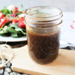balsamic dressing in a jar with a salad behind.