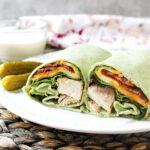 grilled chicken with lettuce on a white plate with pickles besides.