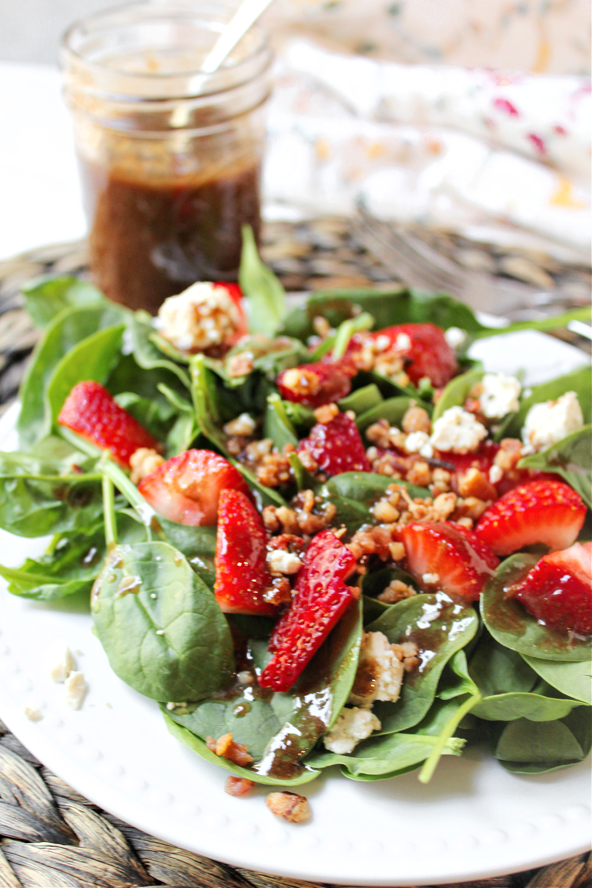 spinach strawberry salad on a plate with dressing behind in a jar.