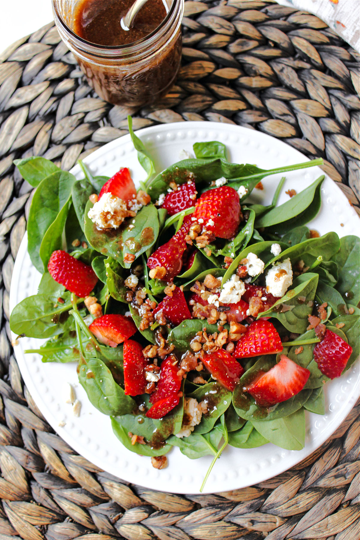 spinach strawberry salad on a white plate with a brown mat underneath. 