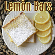 Lemon bars on a white plate with lemons besides.