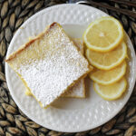 Lemon bars on a white plate with lemons.