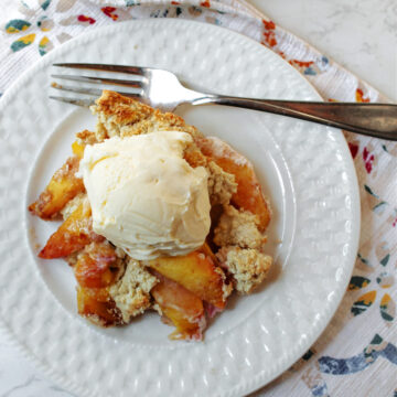 peach cobbler on a white plate with a fork and towel.