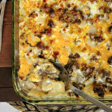 cheesy potato hamburger casserole in a baking dish with a spoon.