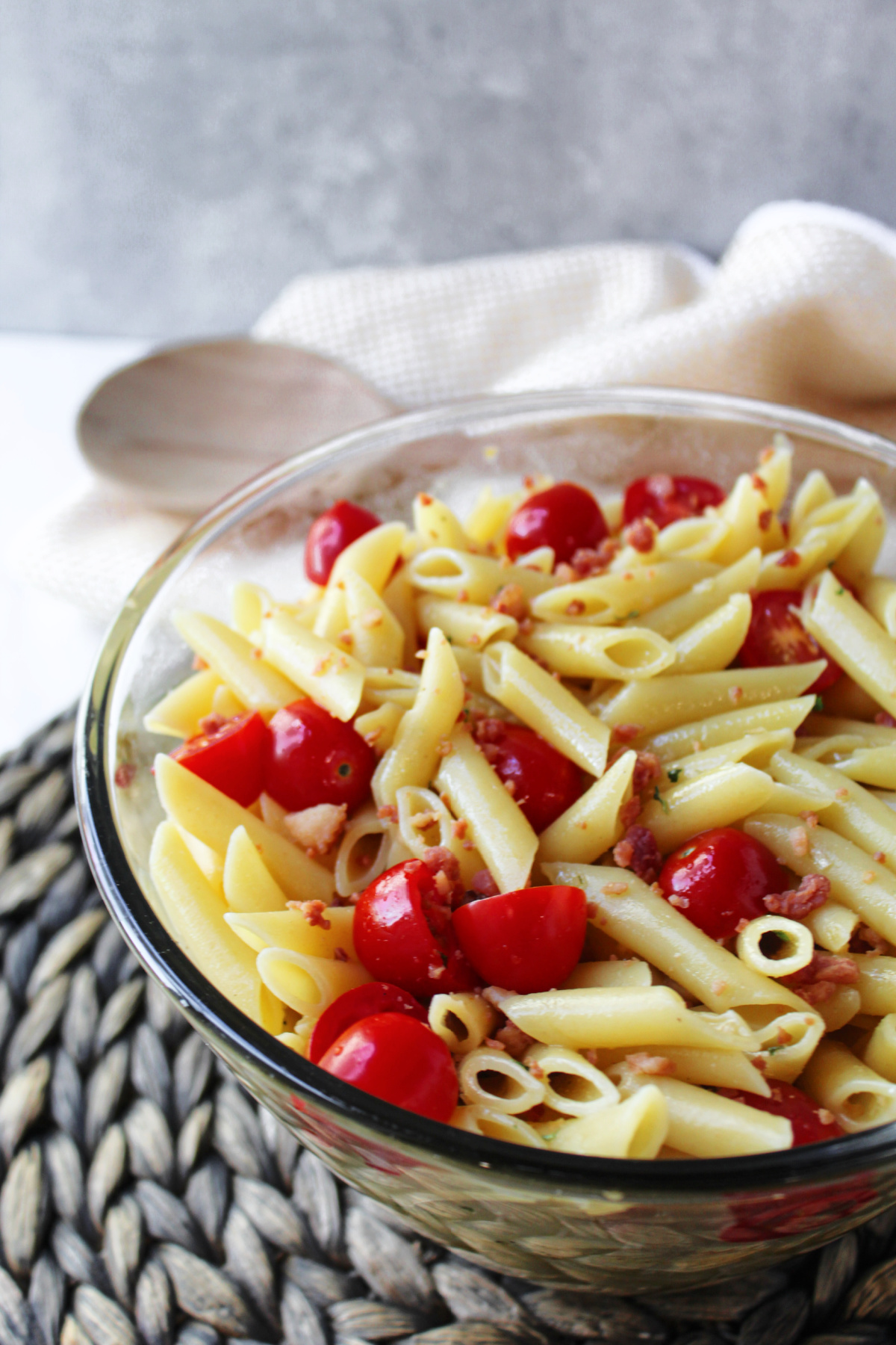pasta salad in a clear bowl with a wooden spoon.