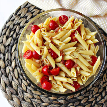 mostaccioli salad in a clear bowl with cherry tomatoes.