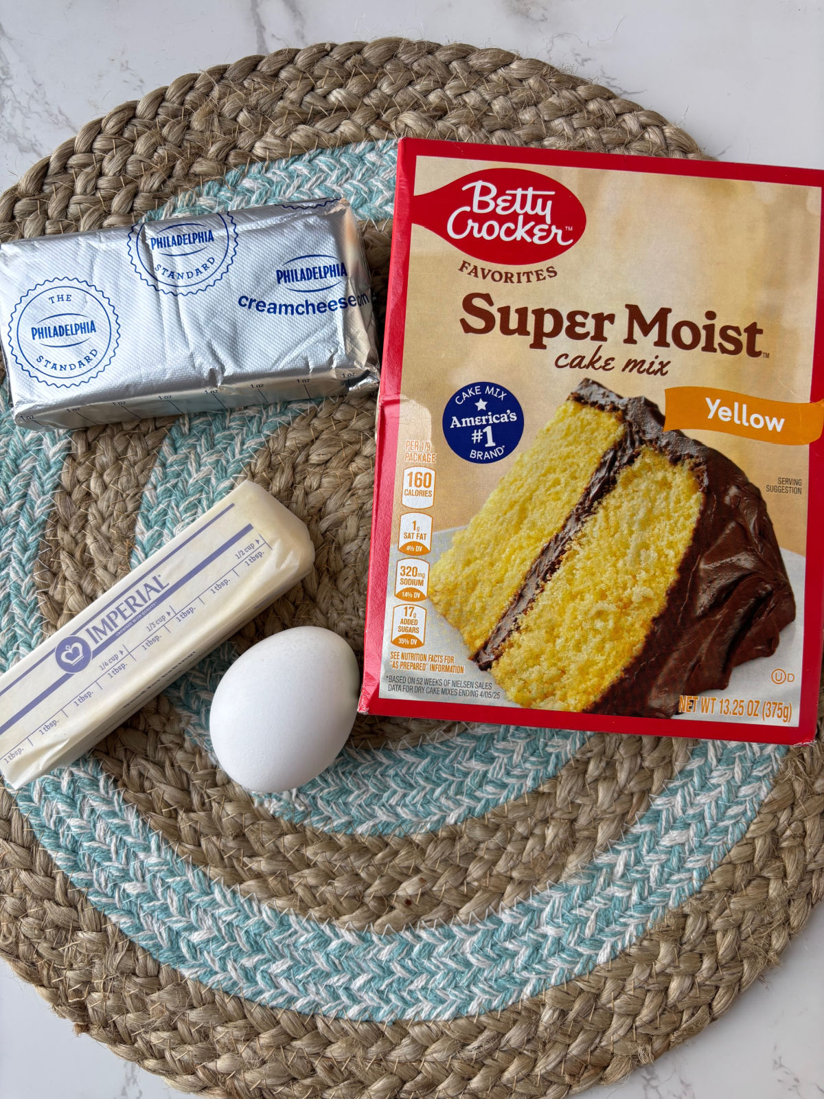 cake mix, egg, butter and cream cheese on a mat.