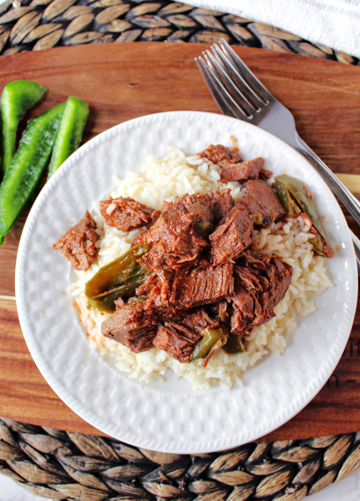Swiss steak on top of rice on a whit plate. 