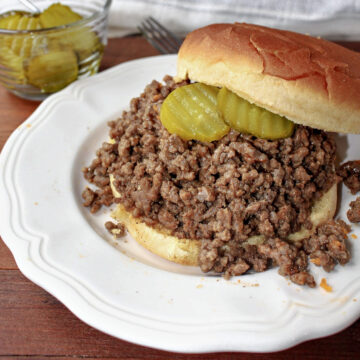 cheeseburger BBQ on a white plate with pickles nearby.
