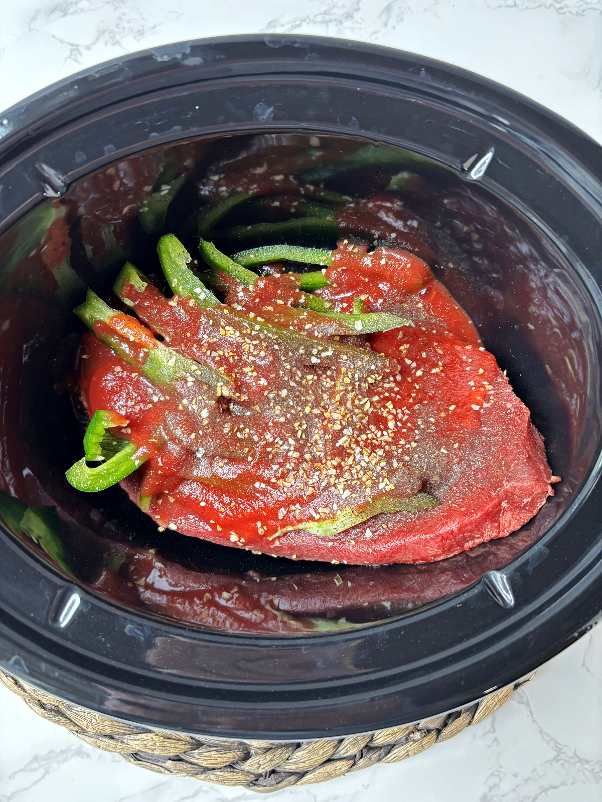 steak in a crock pot with green peppers and tomato sauce.