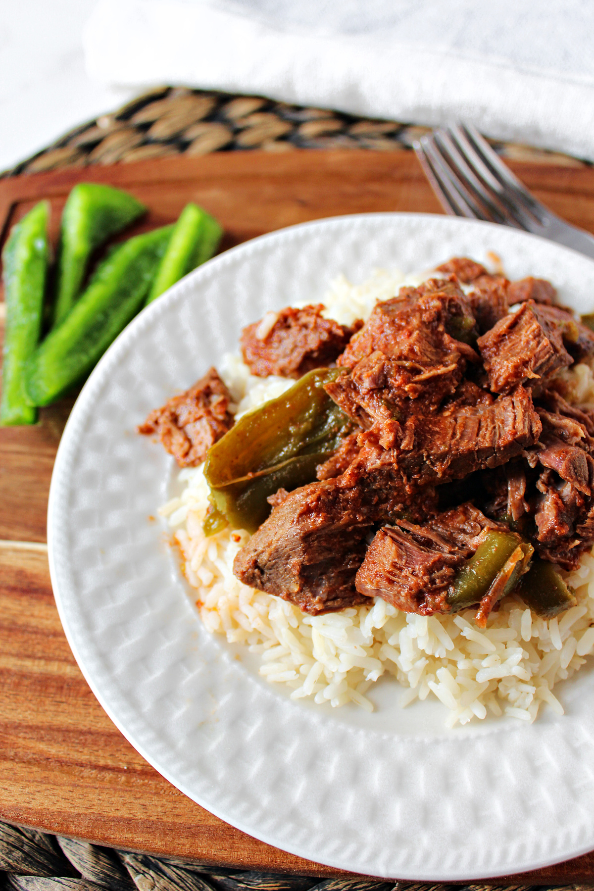 Shredded Swiss Steak on a bed of rice with green peppers nearby.