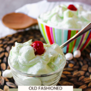 watergate salad in a clear bowl with a spoon and a cherry on top.