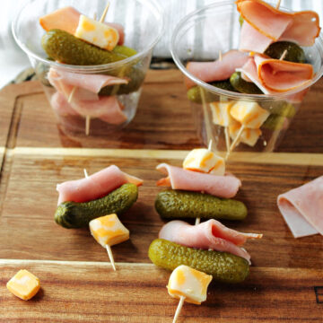 simple ham appetizers with ham, cheese and pickles on a brown tray.