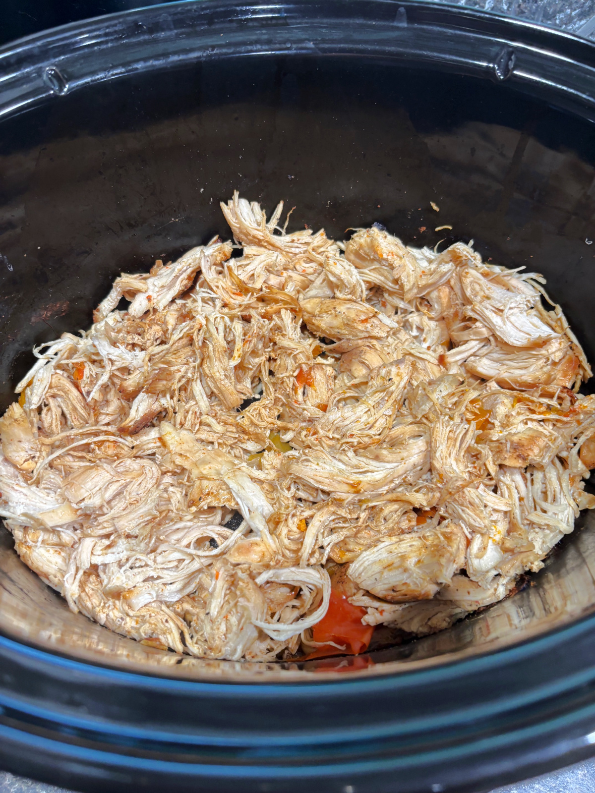 cooked chicken in a crock pot with peppers.