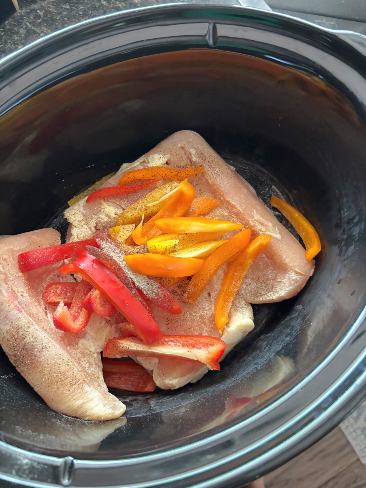 uncrooked chicken in a crock pot with peppers.