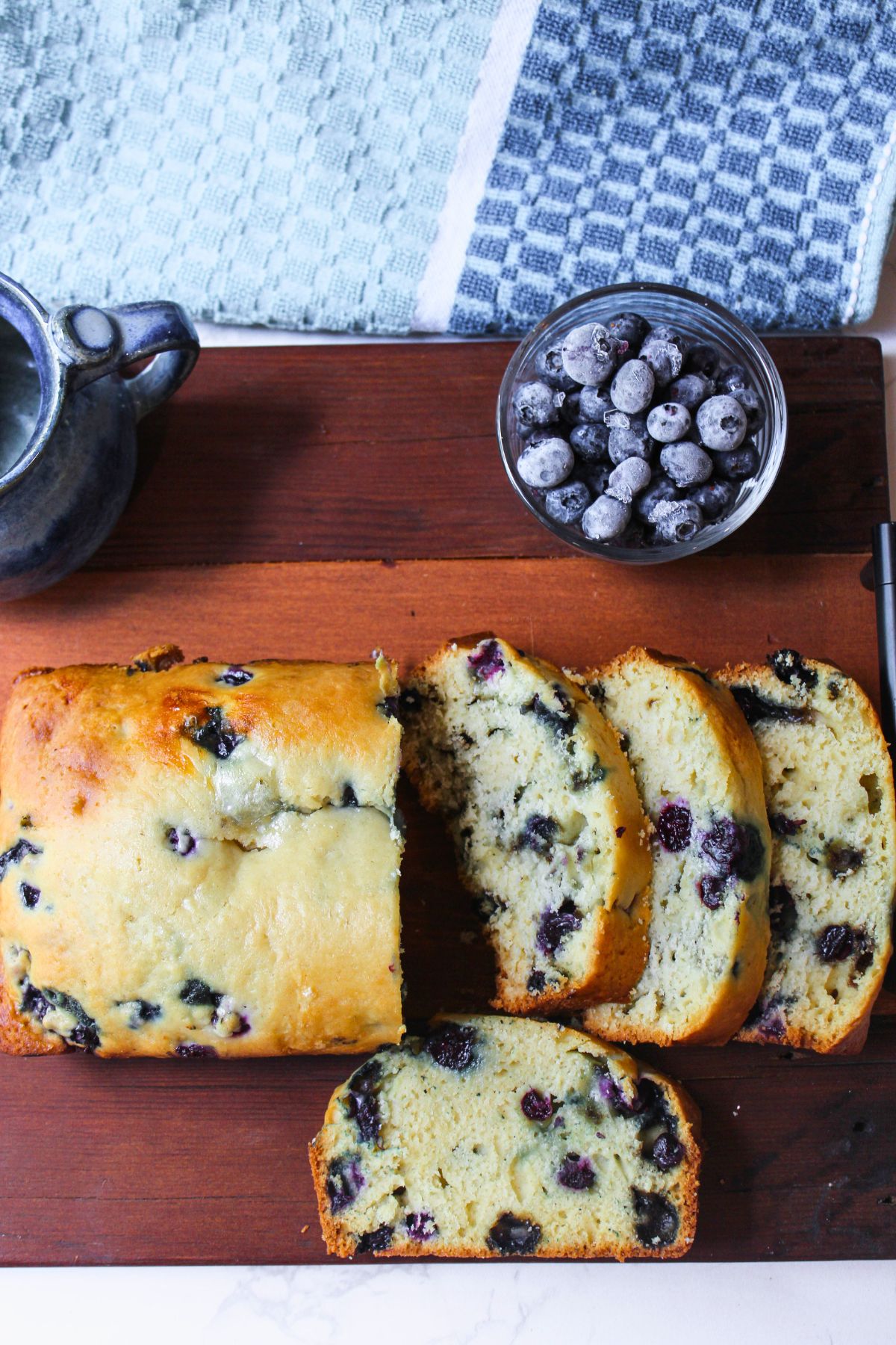 blueberry bread on a wooden tray with blueberries besides. 