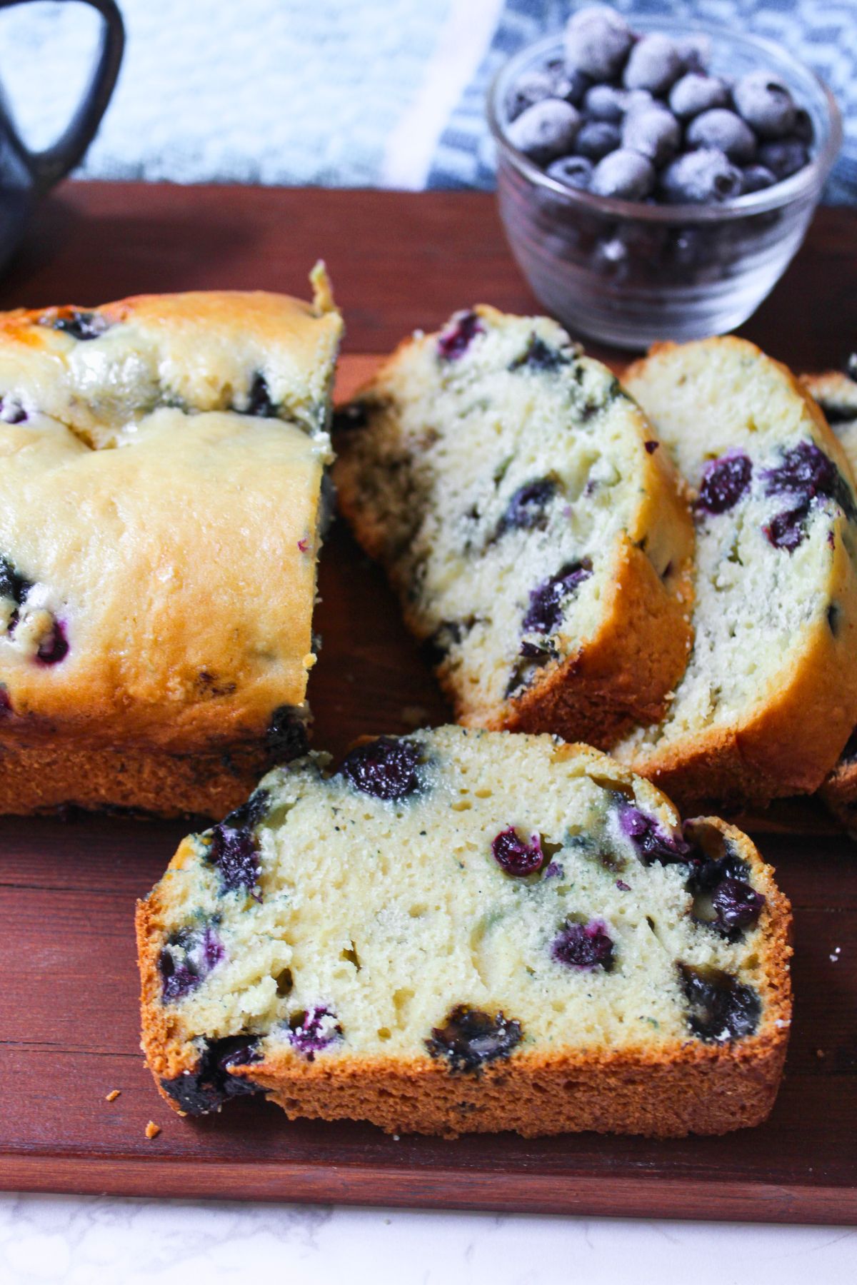 blueberry quick bread with a cup of frozen blueberries nearby.
